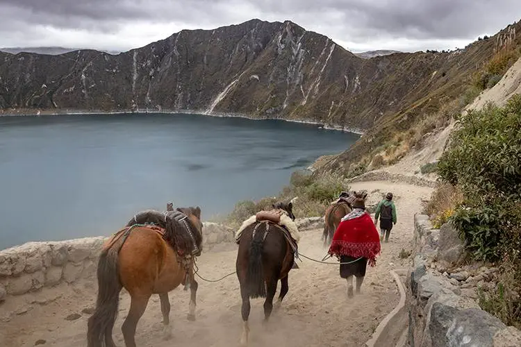 Un grupo de personas montando a caballo por un sendero junto a un lago.