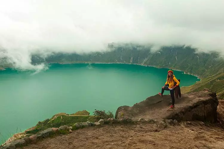 Una mujer parada en la cima de una montaña con vistas a un lago.