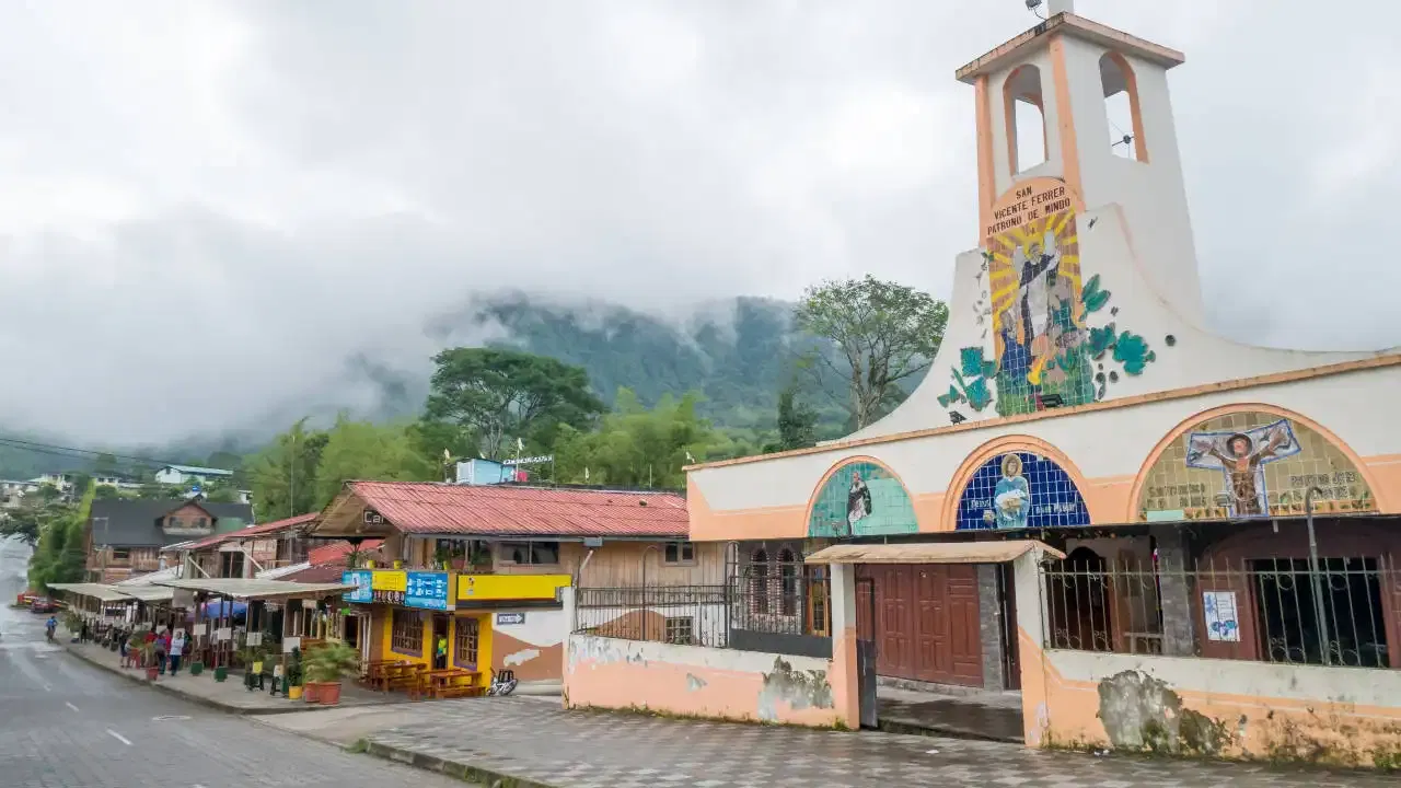 Una calle de un pueblo con una iglesia y monta&ntilde;as al fondo.